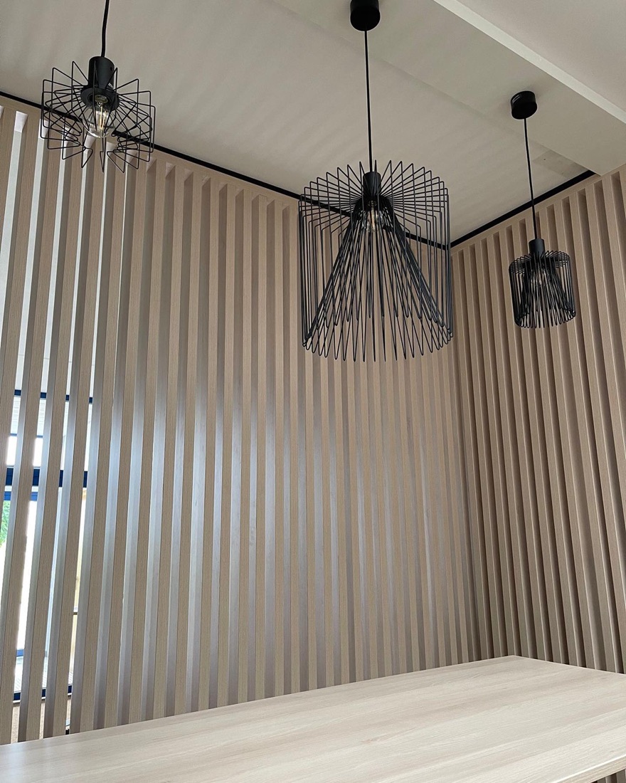 Holzlamellenwand mit schwarzen Drahtpendelleuchten